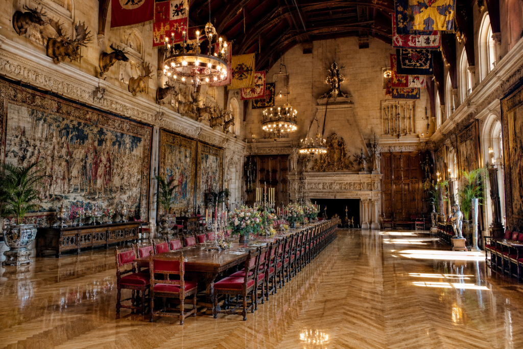 Grand Banquet Hall at Biltmore Estate with a long dining table, soaring ceiling, tapestries, chandeliers, and monumental fireplace.
