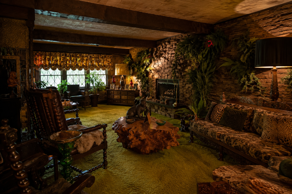 The Jungle Room at Graceland featuring Polynesian-inspired furniture, green shag carpeting, stone walls, and tropical décor