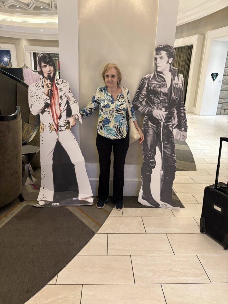 Sylvia standing between two life-sized Elvis Presley cutouts in the lobby of The Guest House at Graceland.